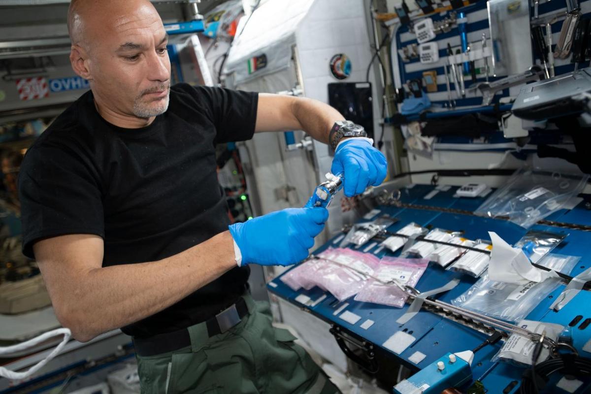 Image of Luca Parmitano wearing blue rubber gloves performing operations for the Amyloid Aggregation investigation examining protein samples for amyloid formation.