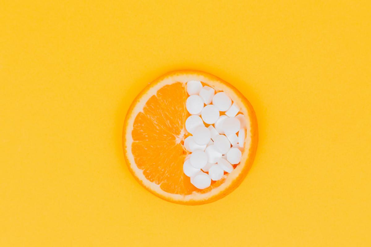 A cut orange covered with white round pills on one half.