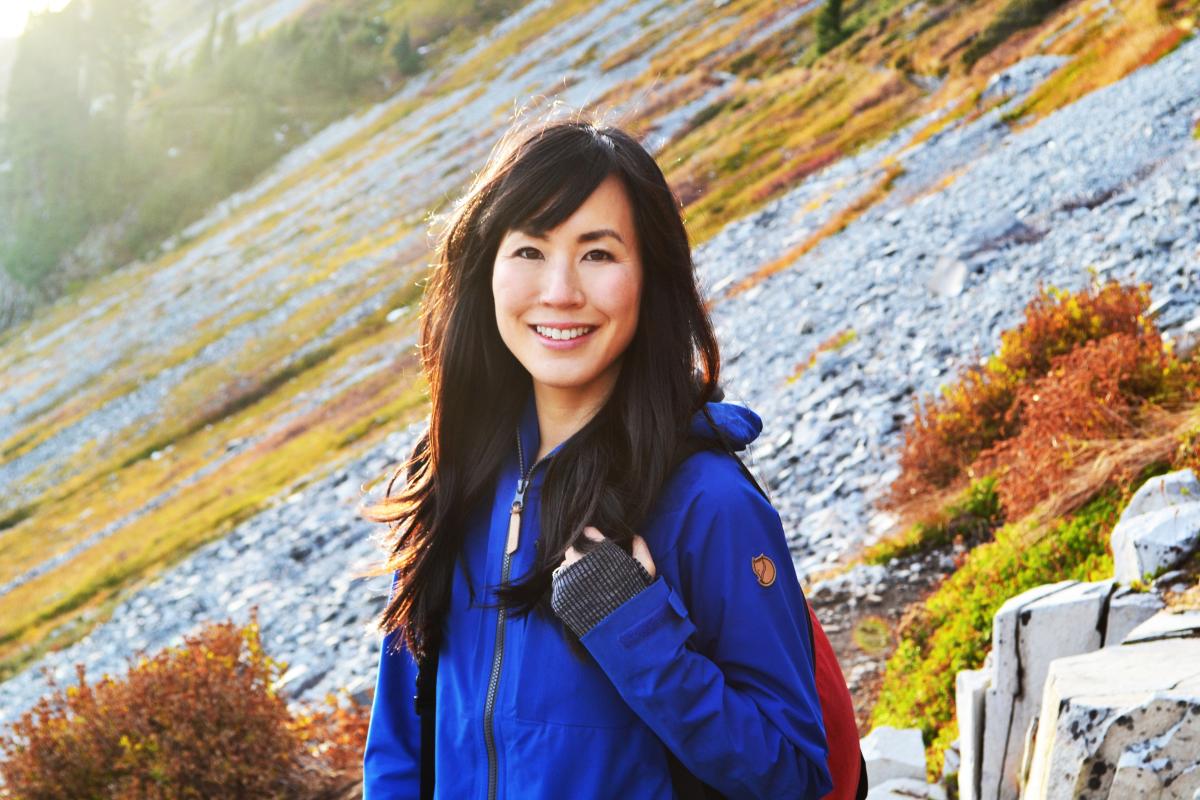Dr Melissa Lem in a blue jacket smiling at the camera, atop a hill.