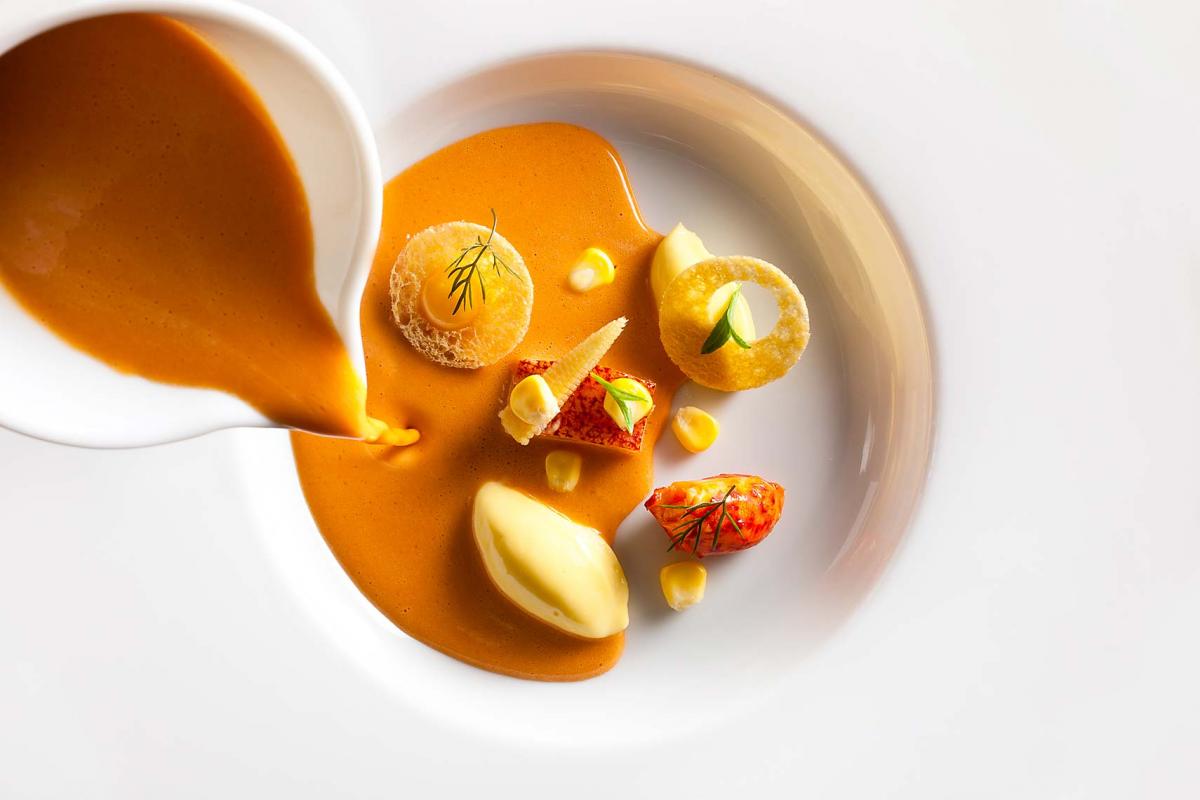Creamy corn soup being poured into a white bowl at Eleven Madison Park Restaurant, NYC