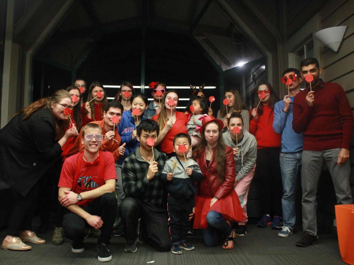 A group of people mostly wearing red clothes holding up paper clown noses and posing for a picture.