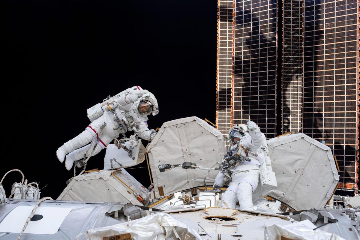NASA spacewalkers (from left) Bob Behnken and Chris Cassidy give a thumbs up during a spacewalk , surrounded by white hardwares and units 