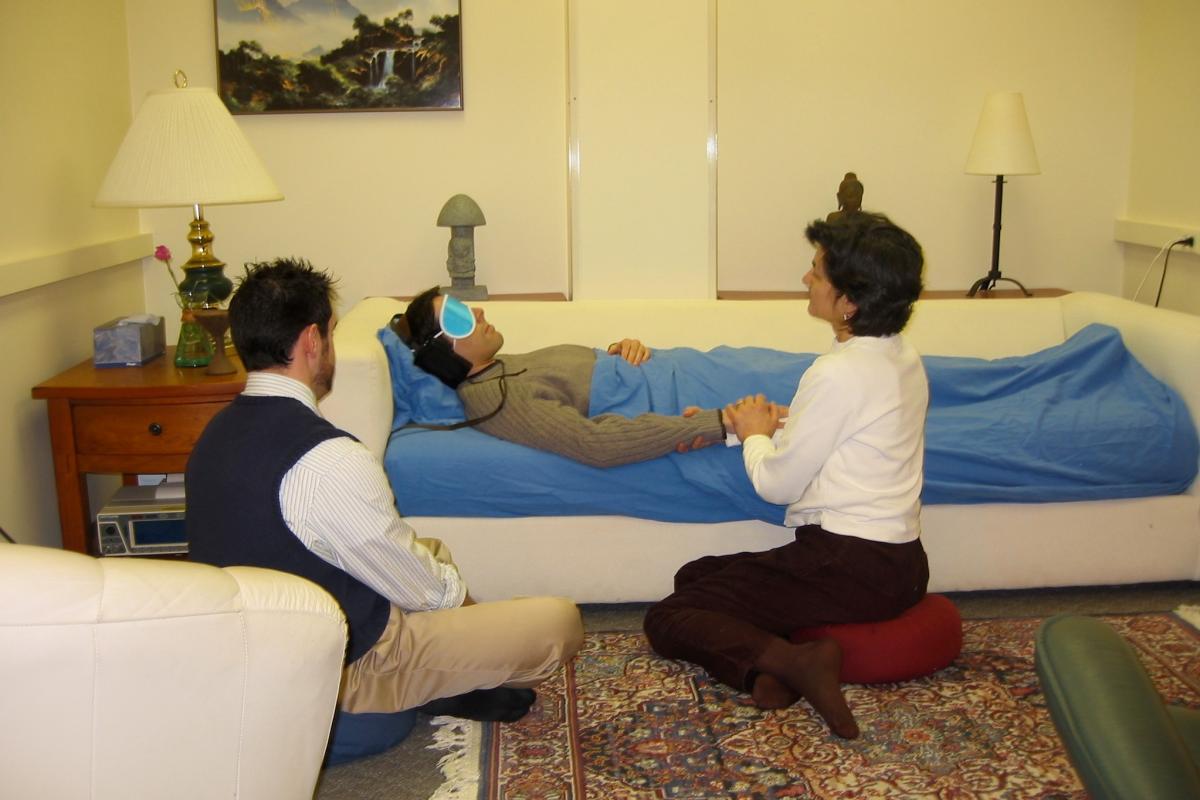 A room with a woman laying on the couch blindfolded with two people assisting her during a psilocybin session at the John Hopkins University.