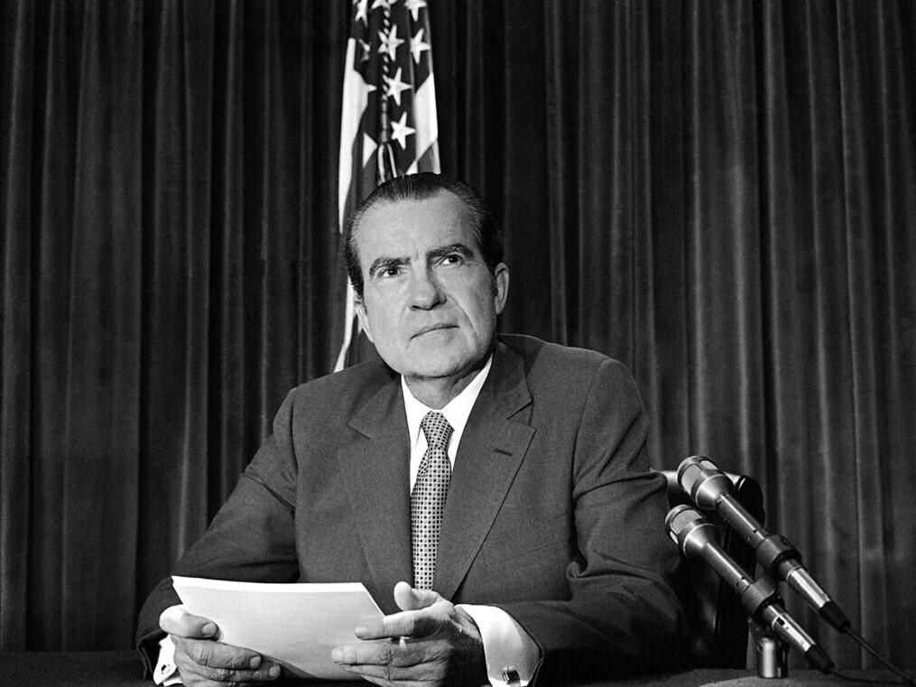 Black and white photo of Richard Nixon sitting on a desk.