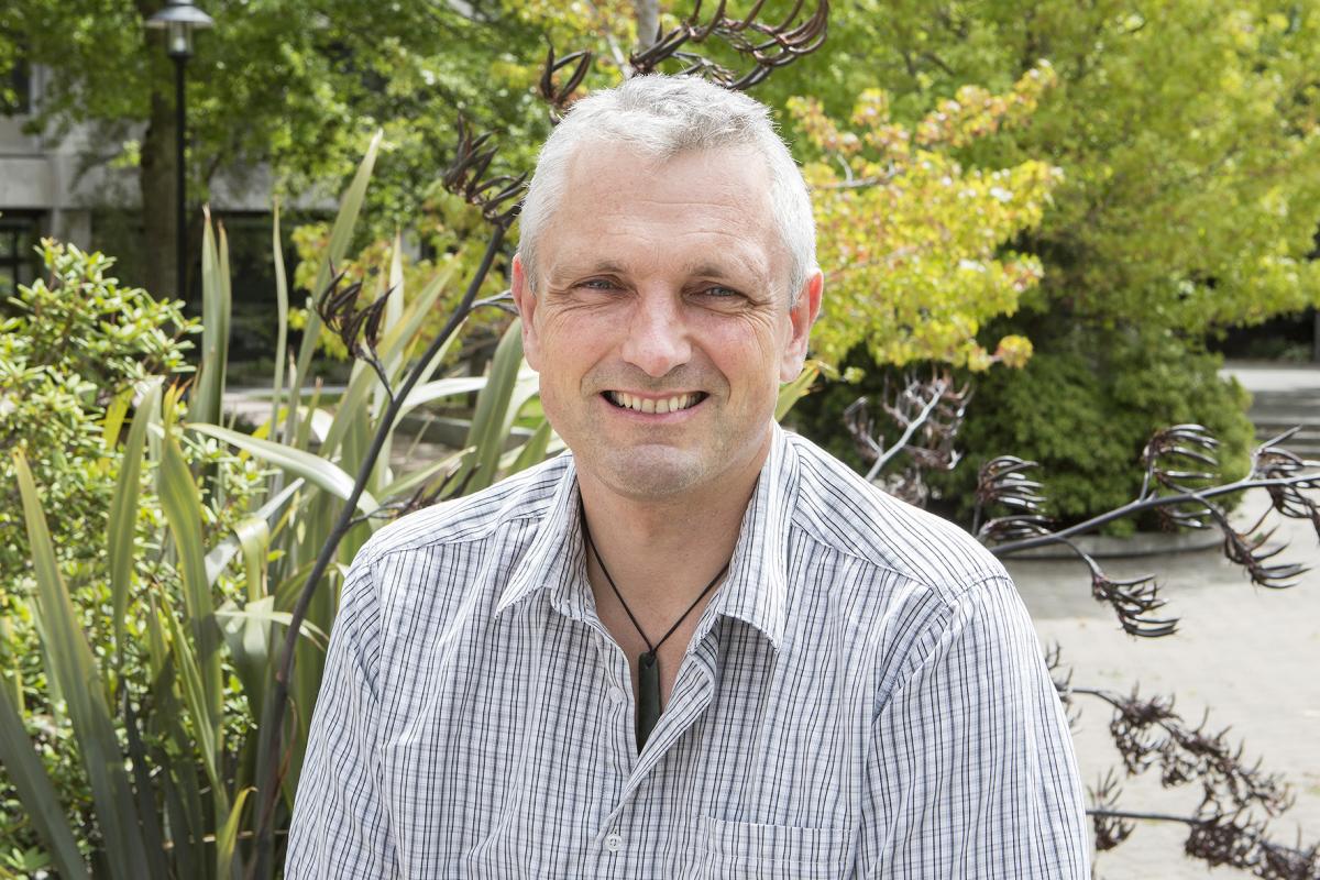 Simon Kingham in a checkered blue shirt smiling at the camera with trees in the background.