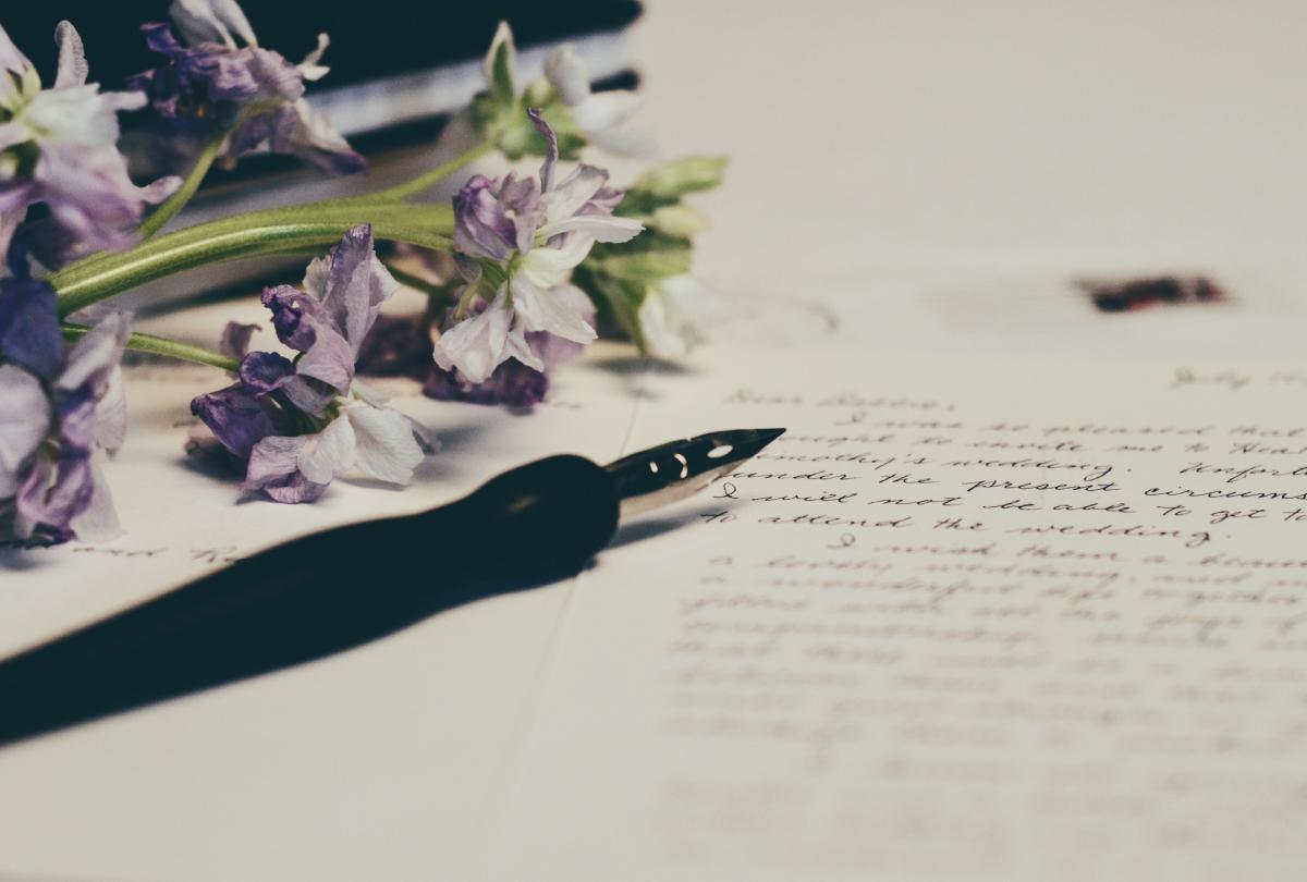 A fountain pen on a paper with handwritten notes with purple flowers on its left.