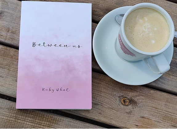 Between us book by Ruby Dhal next to a cup of coffee.
