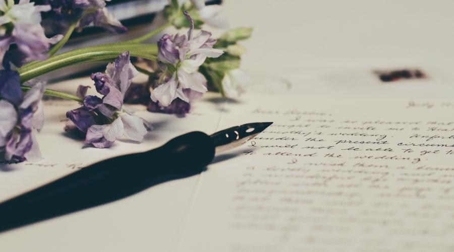 A fountain pen on a paper with handwritten notes with purple flowers on its left.